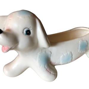 May include: White ceramic planter shaped like a dog with blue and pink accents. The dog has a playful expression and is perfect for small plants.