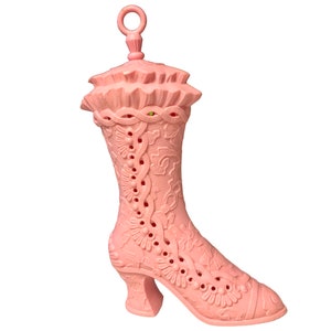 May include: A pink plastic boot-shaped container with a decorative design and a lid. The boot has a high heel and a pointed toe.