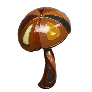 May include: A colorful enamel mushroom brooch with a geometric design in shades of brown, orange, yellow, and red.