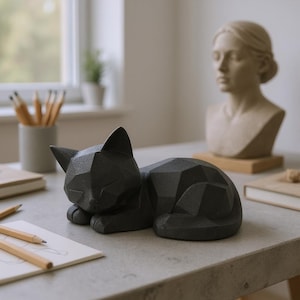 Modern black 3D printed low poly cat sculpture in a sleeping pose on a minimalist desk with art supplies and a bust in the background