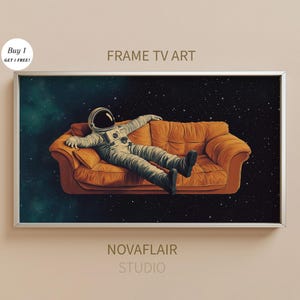 Op de afbeelding: Een ingelijste print van een astronaut die ontspant op een bank in de ruimte. De astronaut draagt een wit ruimtepak en zweeft in een sterrenhemel. De bank is oranje en heeft een wit frame. De print is getiteld "FRAME TV ART" en is van "NOVAFLAIR STUDIO".