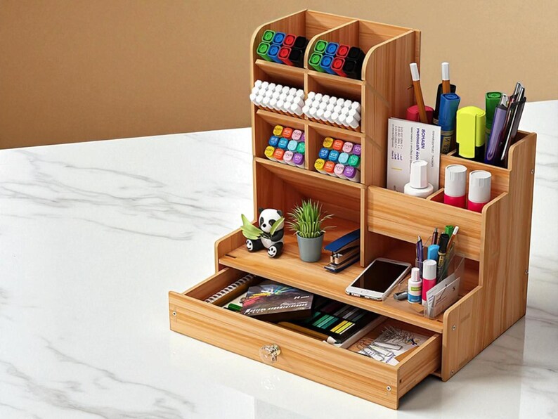 May include: A multi-compartment wooden desk organizer with a drawer. It contains various office supplies, including pens, markers, and small containers. The organizer also holds a small plant, a stapler, and a smartphone. The drawer has a crystal knob.