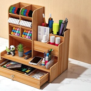 May include: A multi-tiered wooden desk organizer with multiple compartments for pens, markers, and other office supplies. The organizer has a drawer and is filled with various items, including a small panda figurine and a potted plant.