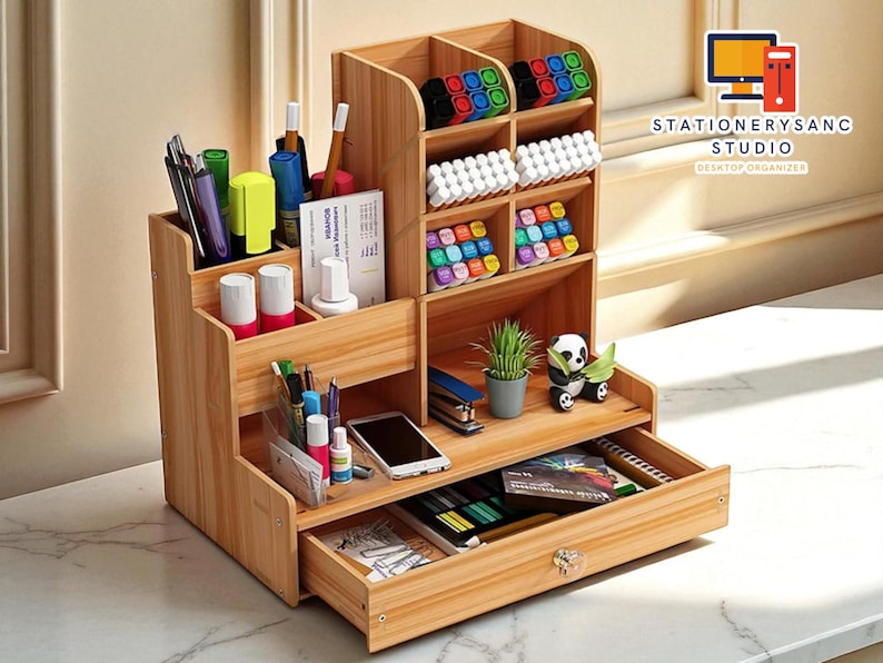 May include: A wooden desk organizer with multiple compartments and a drawer. The organizer is filled with pens, markers, and other office supplies. A small plant and a panda figurine are on the top shelf. The text "STATIONERYSANC STUDIO DESKTOP ORGANIZER" is visible.