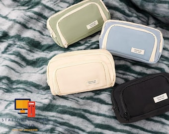 May include: Four zippered pencil cases in different colors: green, light blue, beige, and black. Each case has a zippered pocket and the word "TRAVELER" printed on the front.