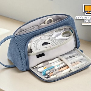 May include: Blue corduroy pencil case with multiple compartments, open to display stationery items. Includes pens, protractor, scissors, and other school supplies. The text "STATIONERYSANC STUDIO DESKTOP ORGANIZER" is visible.