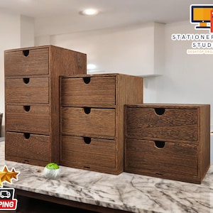 May include: Three wooden drawer organisers in different sizes. The largest organiser has five drawers, the middle organiser has three drawers, and the smallest organiser has two drawers. All of the drawers have a wood grain pattern and are a dark brown colour. The text "STATIONERY SANC STUDIO DESKTOP ORGANISER" is visible in the top right corner of the image.