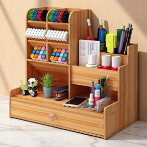 May include: Wooden desk organizer with multiple compartments for pens, markers, and other office supplies. Features a drawer, a small panda figurine, and a potted plant. The organizer is made of light-colored wood.