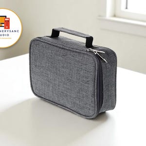 Könnte beinhalten: Ein grauer Desktop-Organizer aus Stoff mit schwarzem Griff und Reißverschluss. Das rechteckige Gehäuse hat abgerundete Ecken und ein strukturiertes Aussehen. Das Produkt stammt von STATIONERYSANC STUDIO, einem Unternehmen für Desktop-Organizer.