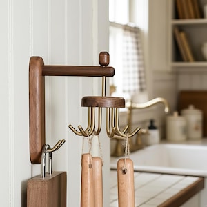 Könnte beinhalten: Ein Küchenutensilienhalter aus Holz mit Messinghaken und einem Schneidebrett. Der Halter ist aus dunklem Holz gefertigt und hat eine horizontale Stange mit einer Reihe von Messinghaken zum Aufhängen von Utensilien.