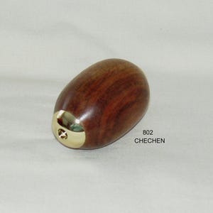May include: A wooden, oval-shaped object with a polished, reddish-brown finish. The base features a gold-colored metal accent. The text "802 CHECHEN" is printed on the surface.