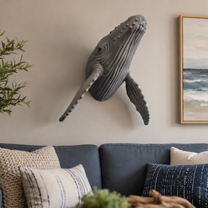 May include: A three-dimensional wall-mounted sculpture of a humpback whale head and pectoral fins. The whale is dark gray with a textured surface showing characteristic throat grooves, bumps on the head, and a realistic eye on the side.