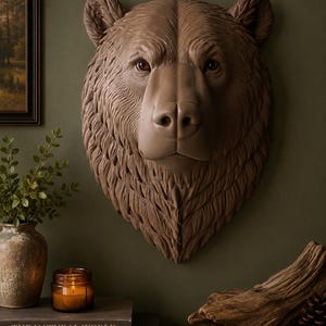May include: A three-dimensional wall-mounted bear head sculpture in a matte brown finish. The piece features detailed fur texture, pointed ears, and realistic eyes, capturing the forward-facing head of a bear with a prominent snout and nose.