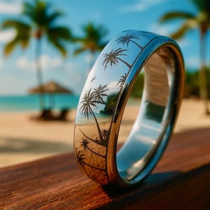 May include: A polished silver ring with a detailed palm tree design. The ring reflects a beach scene with palm trees, sand, and ocean. The ring is set against a blurred background of a beach and blue sky.