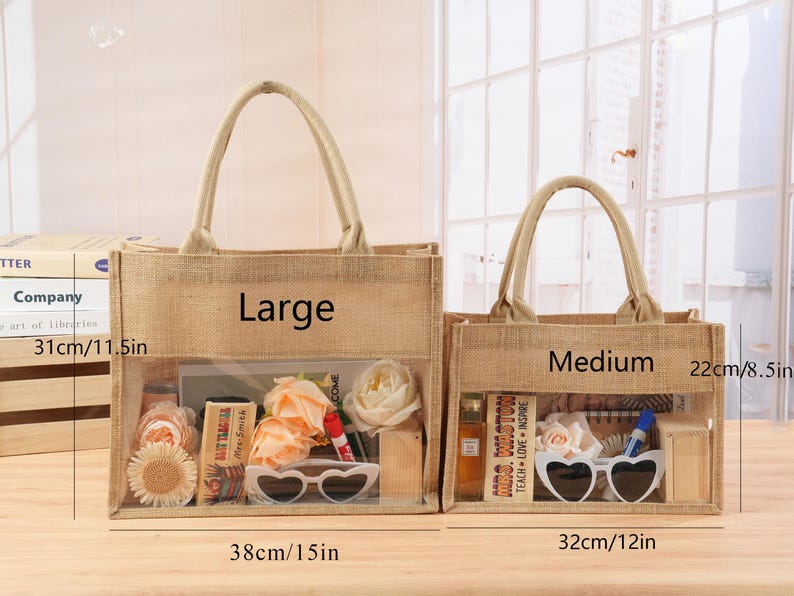 Może przedstawiać: Dwie jutowe torby, oznaczone jako "Large" i "Medium", z przezroczystymi panelami przednimi. Duża torba ma 38 cm szerokości i 31 cm wysokości, a średnia torba ma 32 cm szerokości i 22 cm wysokości. Obie torby zawierają przedmioty.