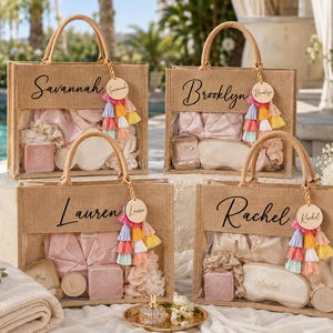 May include: Four rectangular jute tote bags with clear front panels, each personalized with a name in black script. Each bag features a round wooden tag and a multi-colored tassel charm, containing pink and cream satin pajamas, sleep masks, and boxes.
