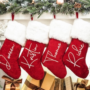 May include: Four red velvet Christmas stockings with white faux fur trim and personalized names in white script: Doreen, Kristin, Thomas, and Richie.