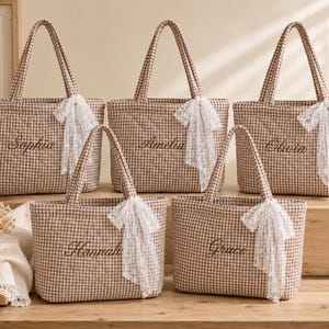 May include: Five quilted tote bags featuring a brown and white gingham pattern. Each bag is embroidered with a unique name: Sophia, Amelia, Olivia, Hannah, or Grace. A white lace ribbon is tied to one of the two handles on each individual tote bag.