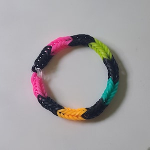 Puede incluir: Una pulsera de goma elástica colorida con bandas negras, rosas, amarillas y verdes tejidas juntas en un patrón.