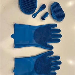 May include: A collection of blue pet grooming tools, including two gloves with textured palms, a brush, a finger brush, and a small oval brush. The tools are made of a flexible, rubbery material.