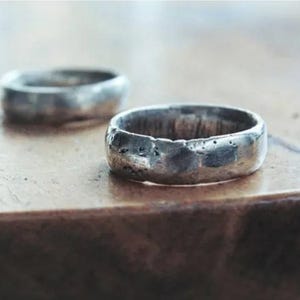 Puede incluir: Dos anillos de plata con textura martillada. Los anillos están sobre una superficie de madera.
