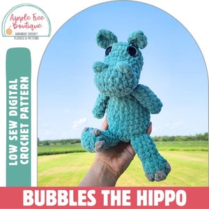 May include: A teal blue crocheted hippopotamus plush toy with black eyes. The toy is being held by a hand against a blue sky background. The text "LOW SEW DIGITAL CROCHET PATTERN" is on the left side of the image and the text "BUBBLES THE HIPPO" is at the bottom of the image.