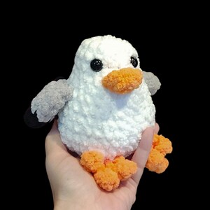 K&ouml;nnte beinhalten: Ein wei&szlig;es, geh&auml;keltes Pl&uuml;sch-M&ouml;wenspielzeug mit orangenen F&uuml;&szlig;en und einem schwarzen und grauen Fl&uuml;gel. Die M&ouml;we hat schwarze Augen und einen orangenen Schnabel.