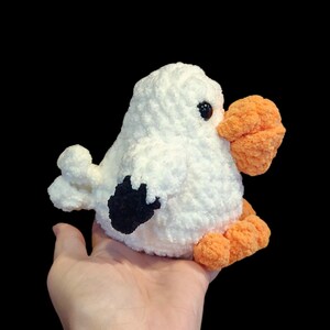 K&ouml;nnte beinhalten: Ein wei&szlig;er geh&auml;kelter Vogel mit schwarzen Augen, einem schwarzen Fl&uuml;gel und orangefarbenen F&uuml;&szlig;en und Schnabel.