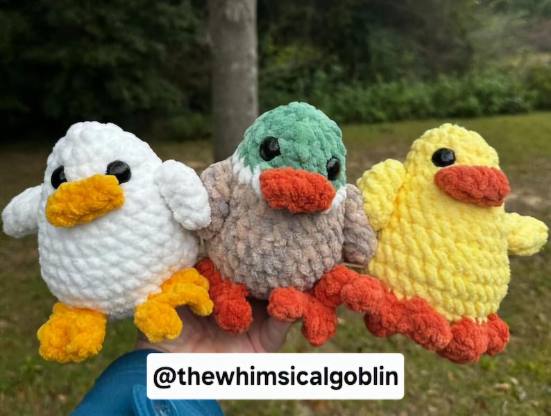 K&ouml;nnte beinhalten: Drei geh&auml;kelte Stofftiere: eine wei&szlig;e Ente, eine gelbe Ente und eine graue Ente mit gr&uuml;nem Kopf und orangefarbenem Schnabel. Die Enten sitzen alle auf einer Hand.