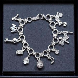Whimsical other world charm bracelet with silver chain and assorted charms including button, key, moon, and odd little storybook inspired details on ldark background