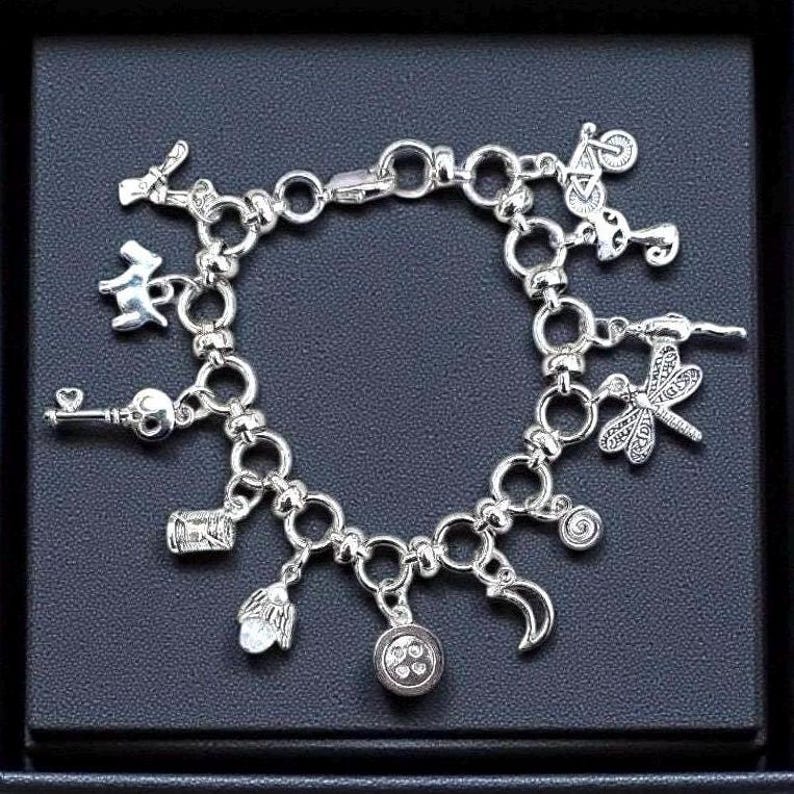 Whimsical other world charm bracelet with silver chain and assorted charms including button, key, moon, and odd little storybook inspired details on ldark background