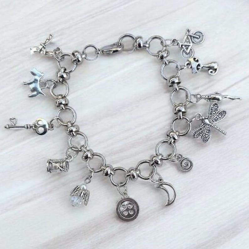 Whimsical other world charm bracelet with silver chain and assorted charms including button, key, moon, and odd little storybook inspired details on light background