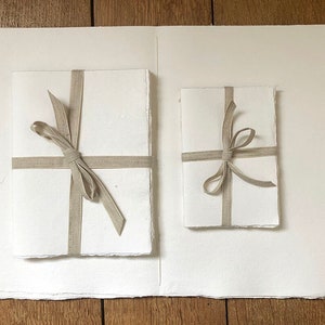 Medium (left) and Small (right) cotton rag paper sketchbooks tied with linen ribbon lie on the open pages of the Large version, against wood background.