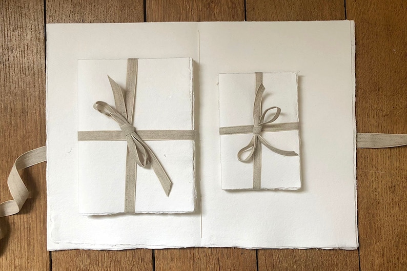 Medium (left) and Small (right) cotton rag paper sketchbooks tied with linen ribbon lie on the open pages of the Large version, against wood background.