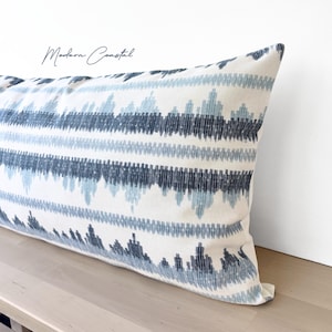 Könnte beinhalten: Ein langes rechteckiges Kissen mit weißem Hintergrund und einem sich wiederholenden Muster aus blauen und marineblauen geometrischen Formen. Das Kissen liegt auf einer hellen Holzoberfläche. Der Text "Modern Coastal" befindet sich in der oberen linken Ecke.