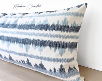 May include: A long rectangular pillow with a white background and a repeating pattern of blue and navy blue geometric shapes. The pillow is resting on a light-colored wooden surface. The text "Modern Coastal" is in the upper left corner.
