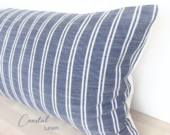 May include: A blue and white striped lumbar pillow with the text "Coastal Linen" printed on the bottom right corner.