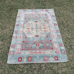 May include: A vintage rug with a light blue background and a geometric pattern in shades of pink, red, and white.