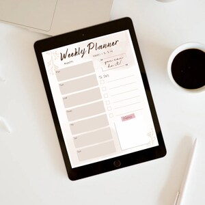 Könnte beinhalten: Ein Wochenplaner auf einem Tablet mit beigefarbenem Hintergrund und floralen Akzenten. Der Planer hat einen Bereich für jeden Tag der Woche mit Platz für To-Do-Listen und Notizen. Der Text "you can do it!" ist in einem rosa Kasten in der oberen rechten Ecke des Planers geschrieben.
