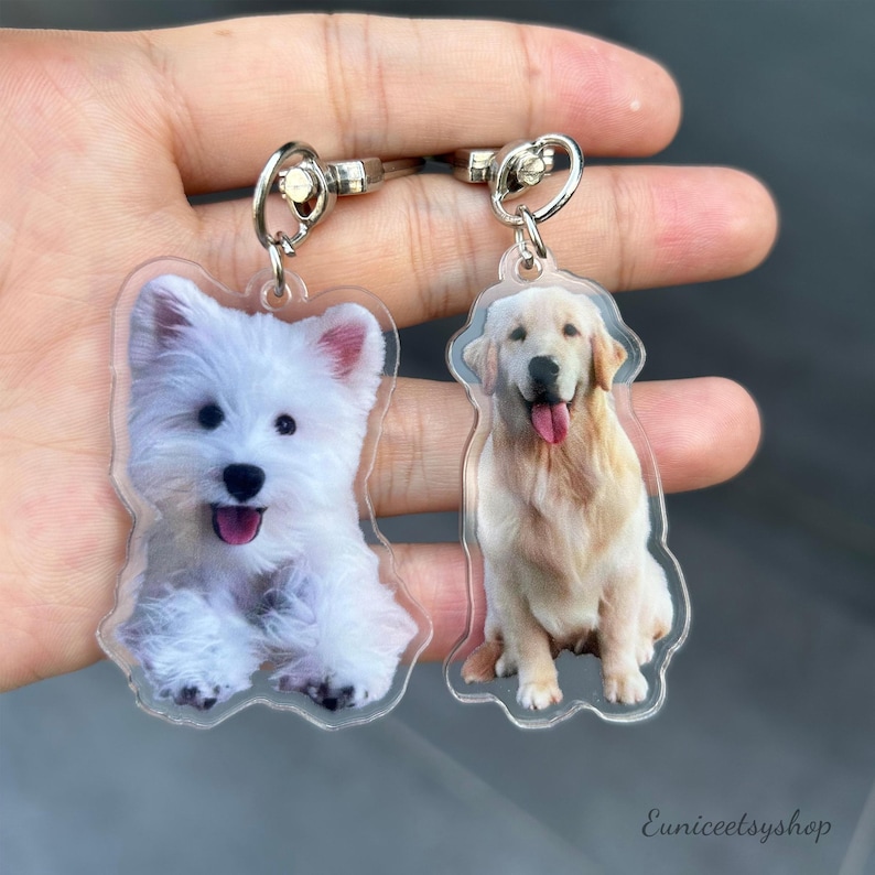 May include: Two clear acrylic keychains with dog photos. One keychain features a white West Highland White Terrier, the other a golden retriever.