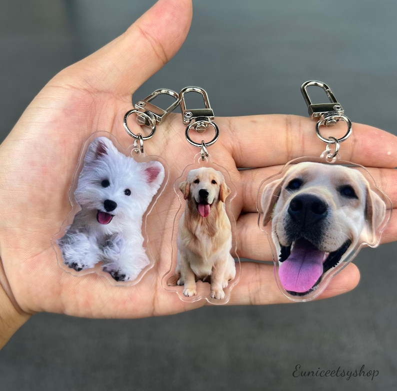 May include: Three clear acrylic keychains with dog photos. The keychains feature a white West Highland Terrier, a golden retriever, and a Labrador Retriever.