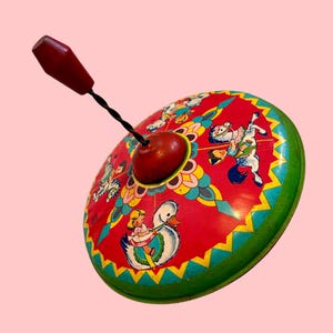 May include: A vintage metal spinning top toy featuring a red base with colorful illustrations of children riding a white swan and a horse. The toy has a central red knob and a black twisted metal handle topped with a red wooden grip for spinning.