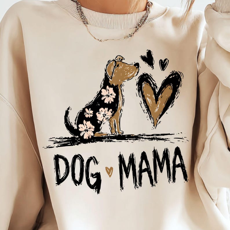 May include: Cream-coloured sweatshirt with a dog illustration and heart design. The dog has floral patterns, and the text "DOG MAMA" is printed below. The design is in a sketched style, with a small heart symbol.