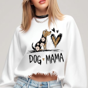 May include: White sweatshirt with a distressed hem. It features a graphic of a dog with floral patterns, a heart, and the text "DOG MAMA" in black. The dog is brown and black, and the heart is brown.