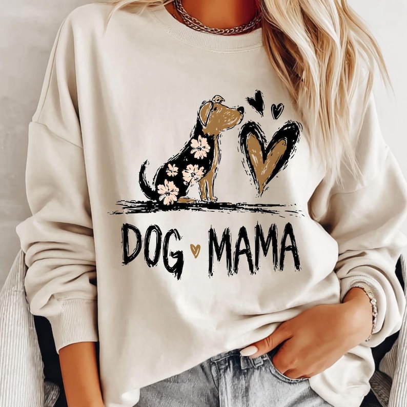 May include: A cream-coloured sweatshirt with a dog illustration, floral accents, and a heart design. The text "DOG MAMA" is printed in black. A casual, comfortable top for dog lovers.