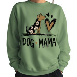 May include: Sage green sweatshirt featuring a dog illustration with floral details, a brown heart, and the text "DOG MAMA". The dog has a brown head and a black body with white flowers.