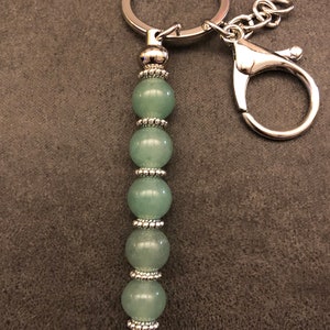 May include: A silver key chain with a green jade bead charm. The charm is made of six round beads with silver accents.