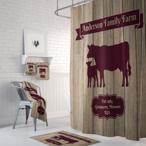 May include: A brown and tan shower curtain with a wood grain pattern. The curtain features a burgundy silhouette of a cow and calf with the text "Anderson Family Farm" and "Est. 1984 Greenacres, Missouri USA".