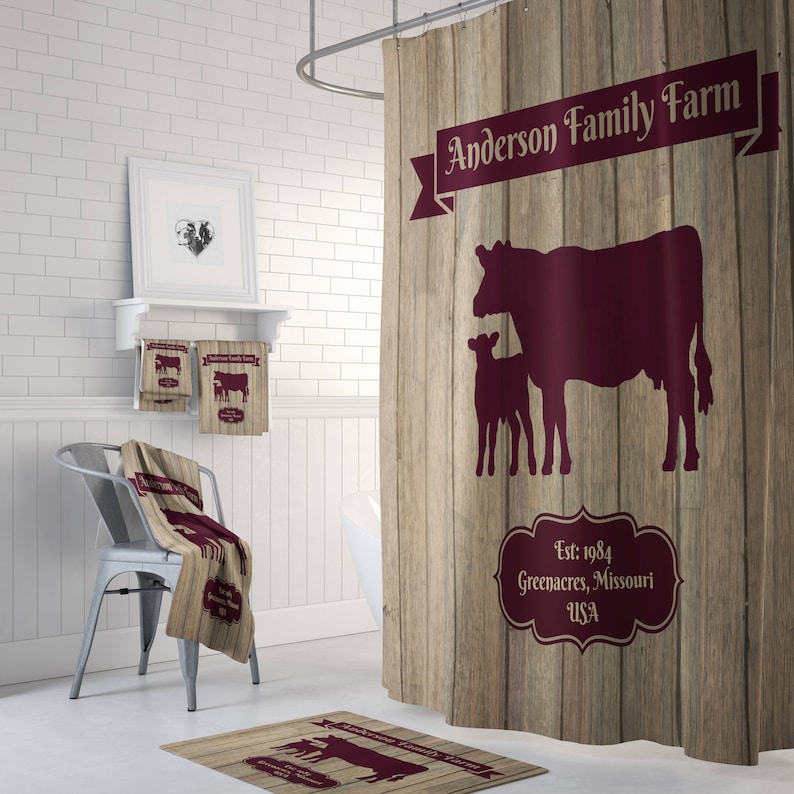 May include: A brown and tan shower curtain with a wood grain pattern. The curtain features a burgundy silhouette of a cow and calf with the text "Anderson Family Farm" and "Est. 1984 Greenacres, Missouri USA".