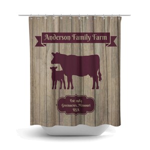 May include: A brown wooden shower curtain with a burgundy silhouette of a cow and calf. The text "Anderson Family Farm" is in a burgundy banner at the top. The text "Est. 1984 Greenacres, Missouri USA" is in a burgundy oval at the bottom.
